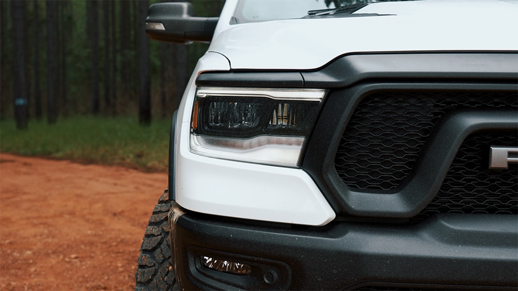 The right headlight of a white RAM Rebel 1500 G/T on a dirt road.